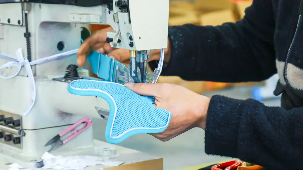 A clean, brightly lit, modern manufacturing facility showing a skilled worker using advanced sewing machinery to assemble a pet harness, with a subtle focus on precision and strict quality control.